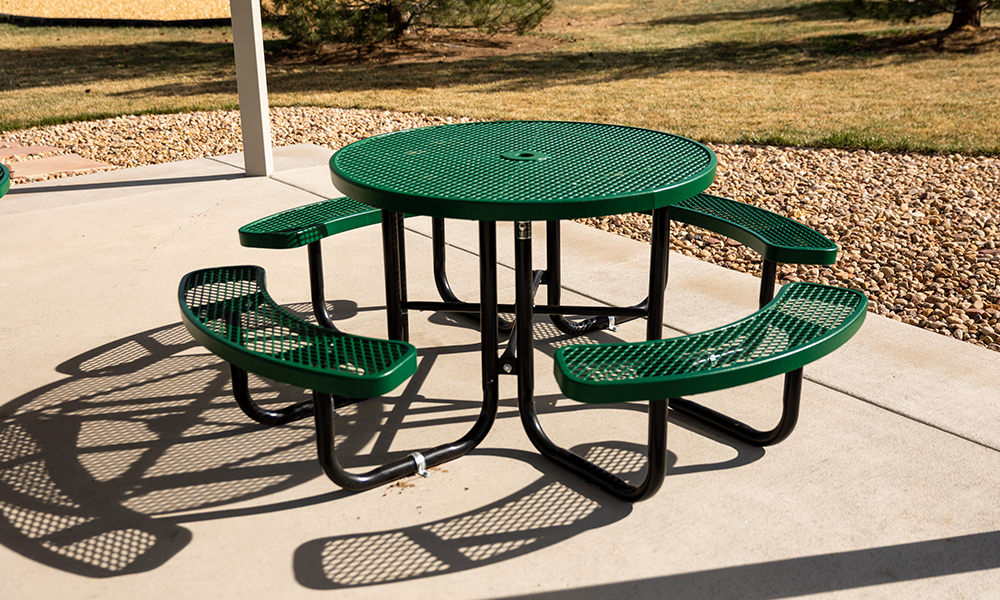 Round expanded metal pedestal picnic table with curved benches and surface mount frame for commercial outdoor seating areas
